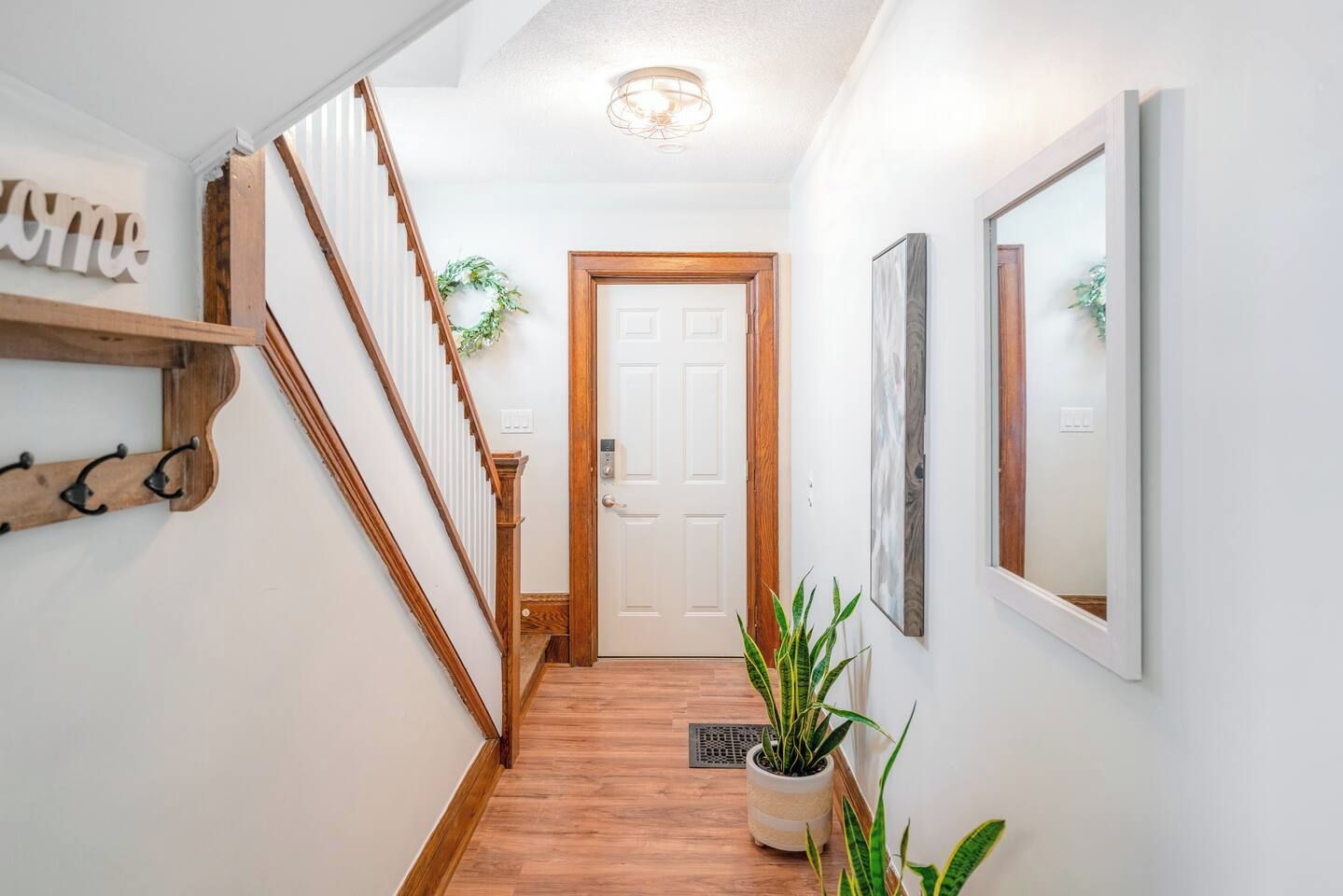 A hallway with a wooden staircase, a coat rack, a door, and a potted plant.