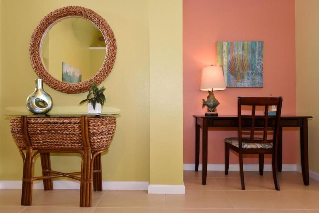 A room with a wicker chair, a table, a lamp, and a mirror on the wall.