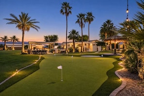 Un campo de golf con una bandera, palmeras y un edificio con terraza.