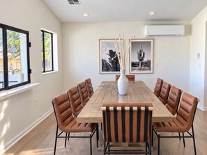 Un comedor con una mesa de madera rodeada de sillas de cuero, cuadros en la pared y un equipo de aire acondicionado en lo alto.