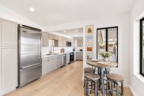 A modern kitchen with stainless steel appliances, light wood flooring, and a dining area with stools. - 19 Bds+Volleyball+Pickleball+Sauna+Cold Pl+Events (Indio)