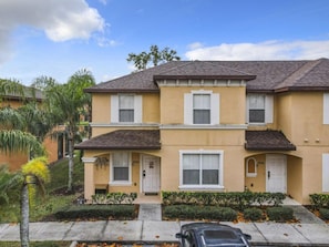 A two-story residential building with a flat roof, white-framed windows, and a beige exterior. - Family Getaway 4BR Townhome by Old Town (Kissimmee)