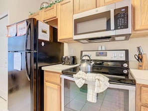 A kitchen with a black refrigerator, a microwave, an oven, and a kettle. - Family Getaway 4BR Townhome by Old Town (Kissimmee)