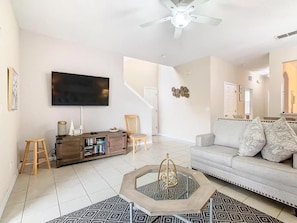 A living room with a flat-screen TV, a sofa, a coffee table, and a staircase leading to another room. - Family Getaway 4BR Townhome by Old Town (Kissimmee)