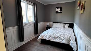 Un dormitorio con cama, ventana con cortinas, lámpara de pared y radiador.