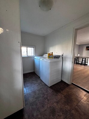 Una sala amb rentadora i assecadora, una finestra i una porta que dona a una altra habitació.