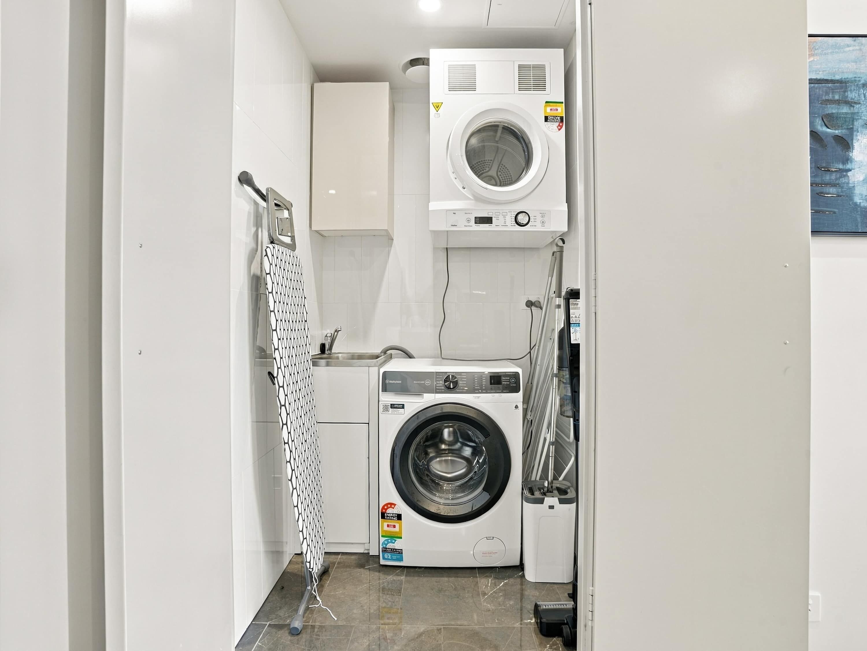 Une petite buanderie équipée d’un lave-linge et d’un sèche-linge à chargement frontal, d’un étendoir et d’un petit évier.