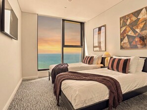 A hotel room with a large window offering a view of the sea, a bed with a dark headboard, and a painting on the wall. - The Mojo Sky Suite, Sunrise Ocean View, Meriton (Surfers Paradise)