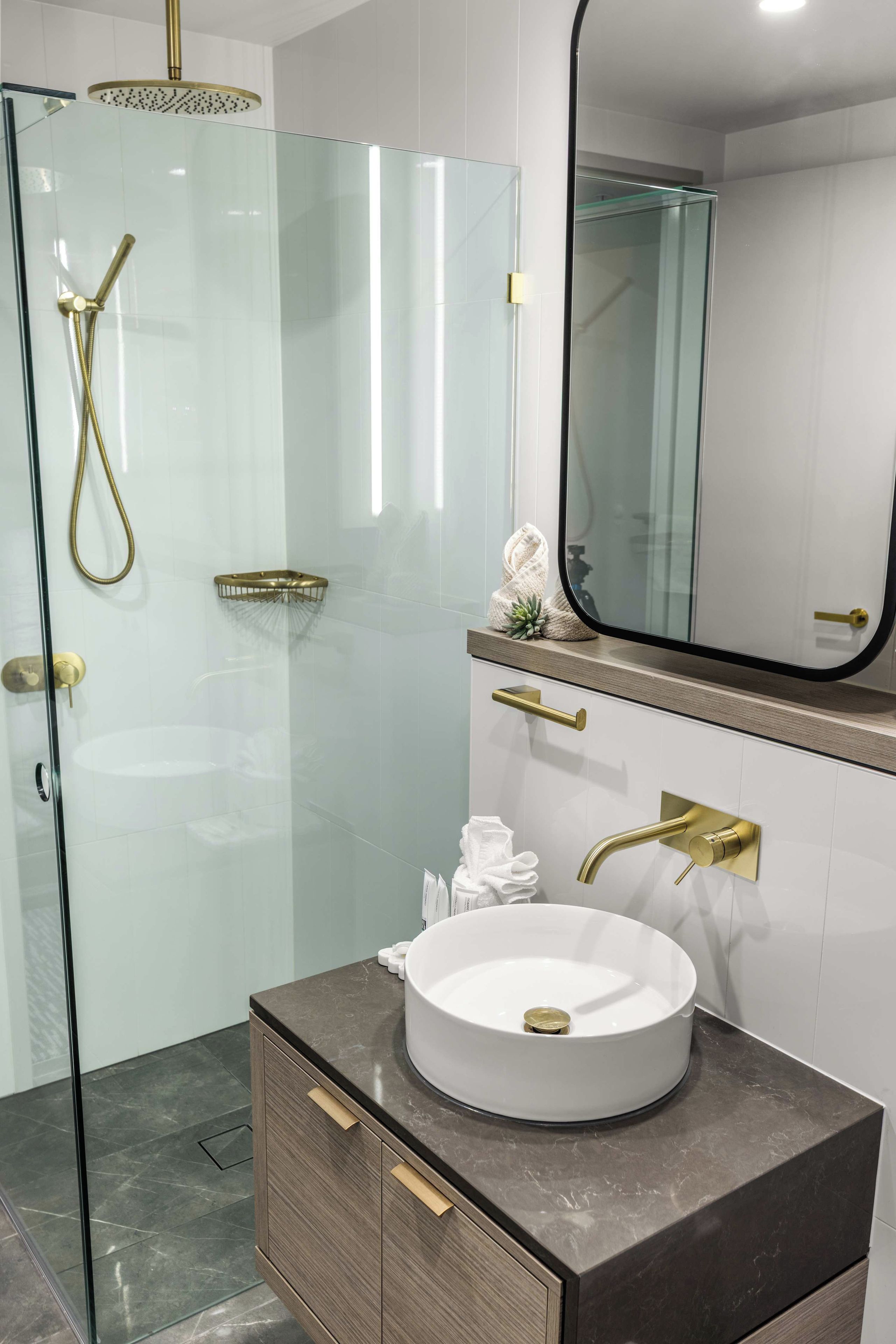 Une salle de bain moderne avec une douche à parois de verre, un lavabo rond blanc et un grand miroir au-dessus du meuble-lavabo.