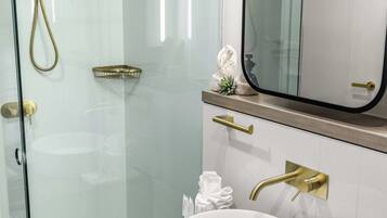 Une salle de bain moderne avec une douche à parois de verre, un lavabo rond blanc et un grand miroir au-dessus du meuble-lavabo.