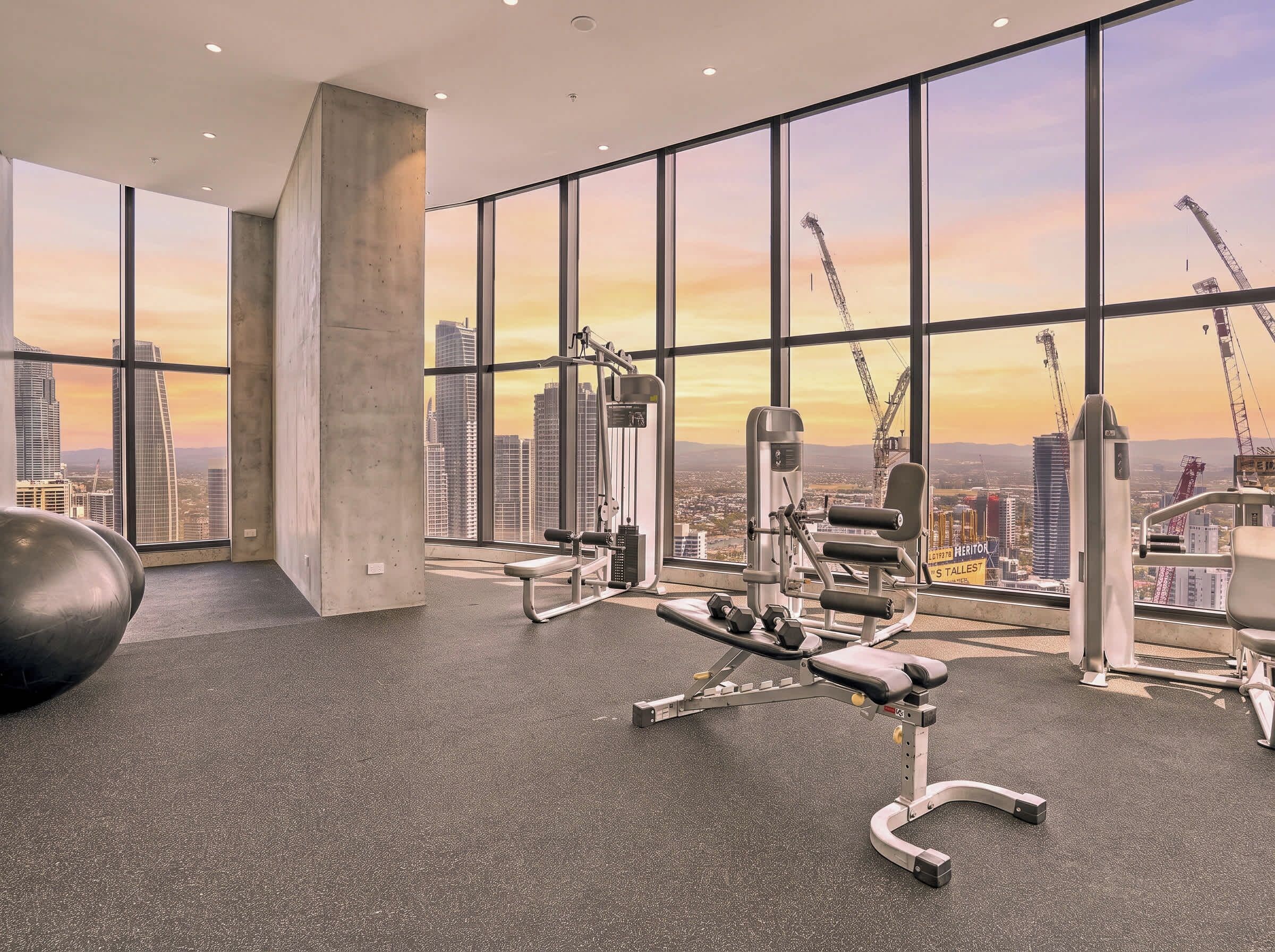 Ein Fitnessstudio mit Trainingsgeräten und großen Fenstern mit Blick auf eine Stadtlandschaft.