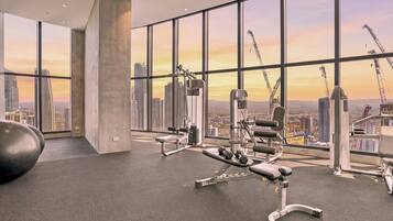Ein Fitnessstudio mit Trainingsgeräten und großen Fenstern mit Blick auf eine Stadtlandschaft.