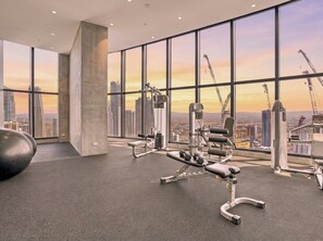 Ein Fitnessstudio mit Trainingsgeräten und großen Fenstern mit Blick auf eine Stadtlandschaft.