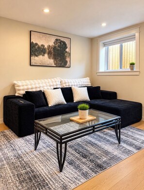 Uma sala de estar moderna com um sofá preto, uma mesa de centro de vidro e um quadro na parede.