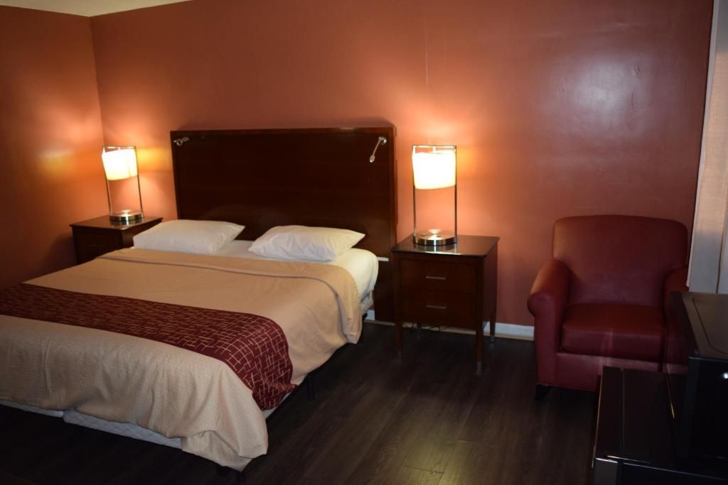 A hotel room with a bed, two bedside tables with lamps, a red chair, and a desk.