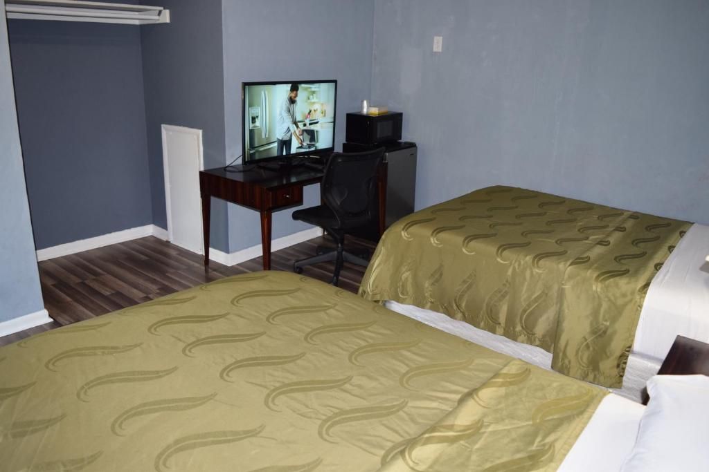 A hotel room with two beds, a desk with a television, and a chair.