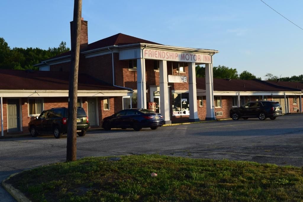 A building with a sign that reads 'FRIENDSHIP MOTOR INN.' There are cars parked in front, and the building has a brick facade with a flat roof.