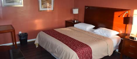 A hotel room with a bed, bedside table, lamp, and artwork on the wall.