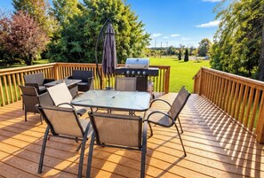 Une terrasse extérieure avec une table et des chaises, un barbecue et une vue sur une zone verdoyante.
