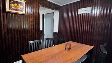 Un salón de conferencias con una mesa de madera, sillas negras, un ventilador de techo y un cuadro en la pared.
