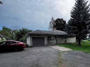 Une maison de plain-pied avec un garage, une allée et une voiture rouge garée devant.