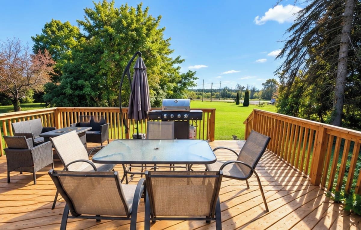 Une terrasse avec une table à plateau en verre, des chaises et un barbecue.