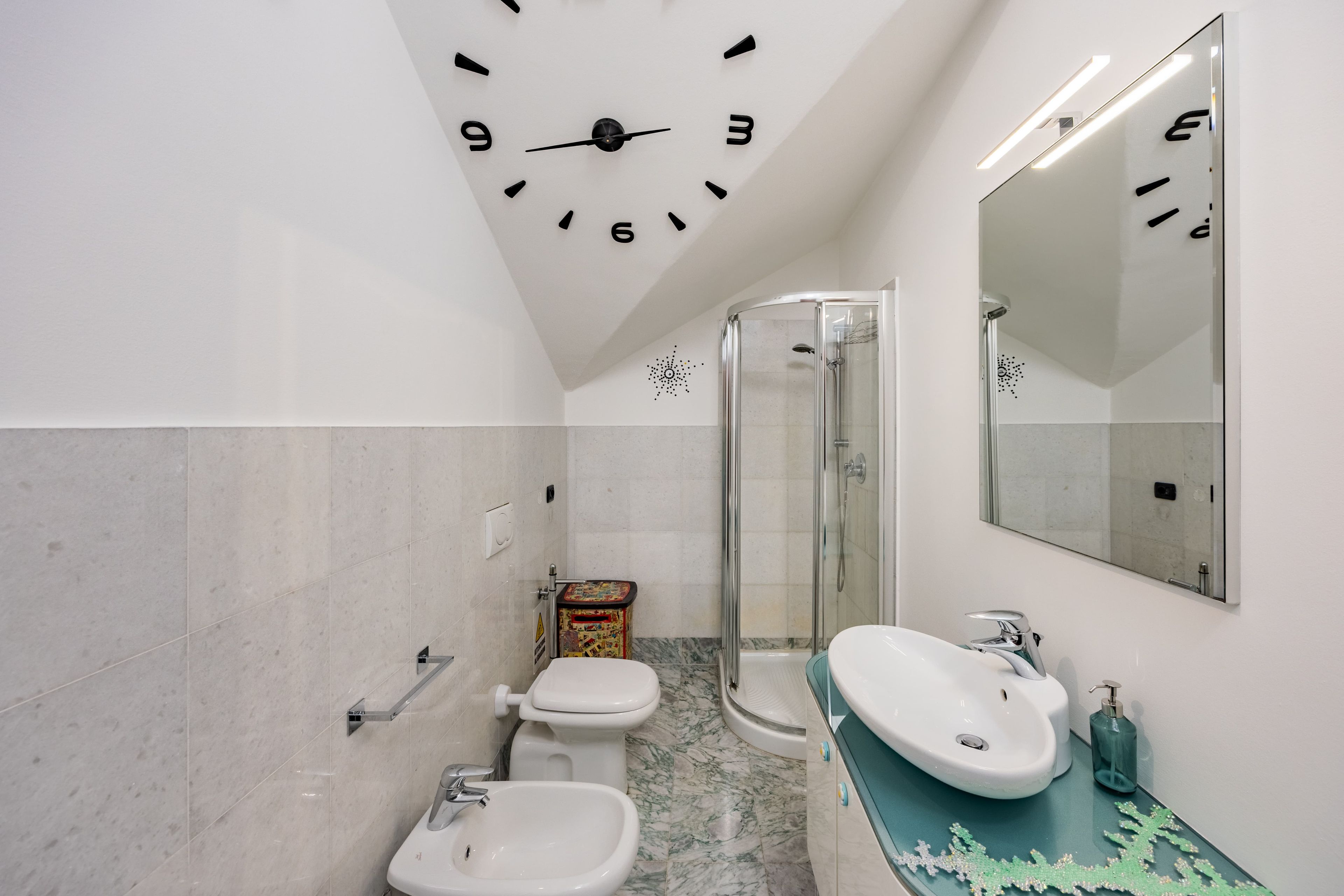 Un bagno con orologio a parete, doccia, WC e lavandino.