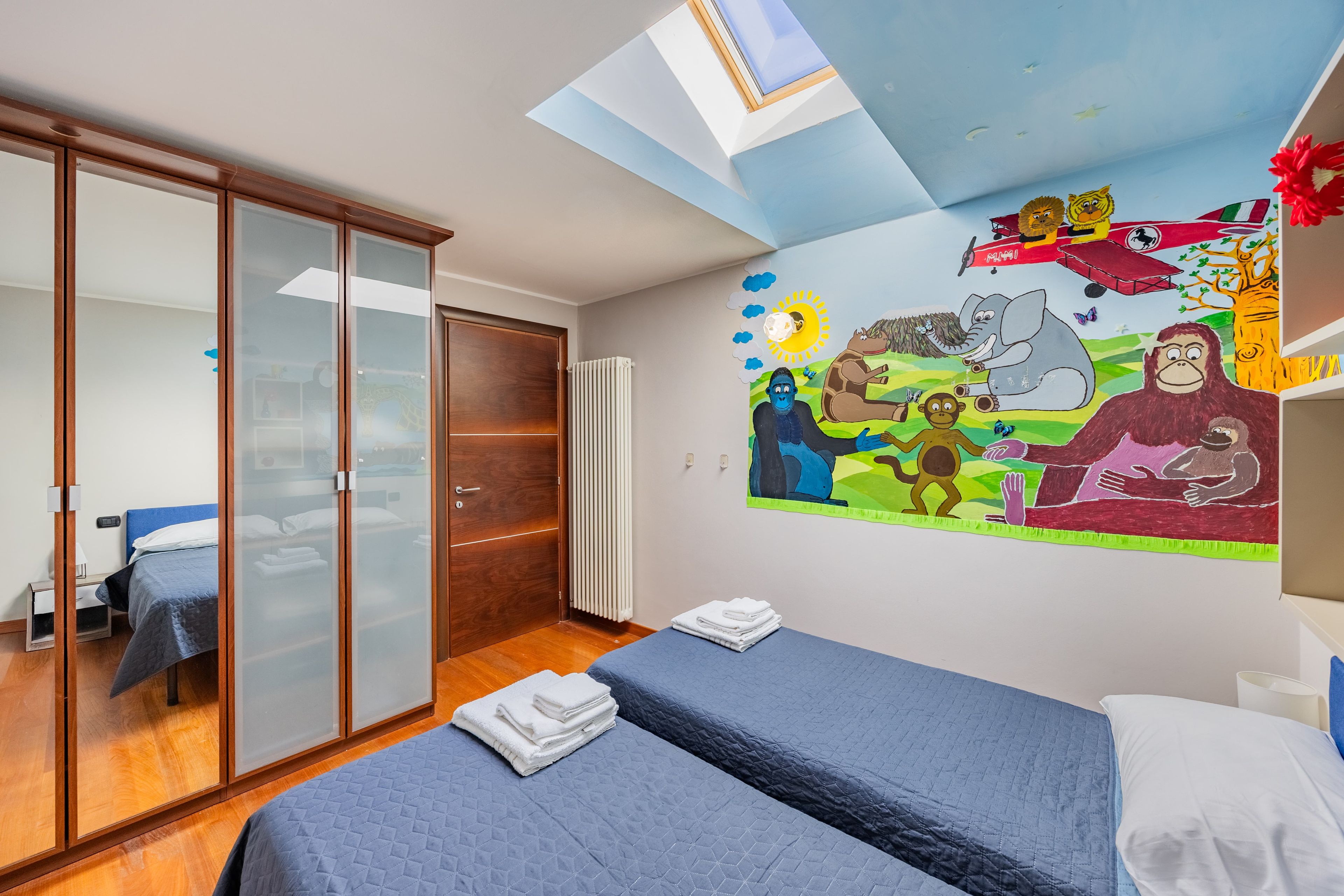 Een slaapkamer met een bed, een kledingkast, een radiator en een muurschildering.