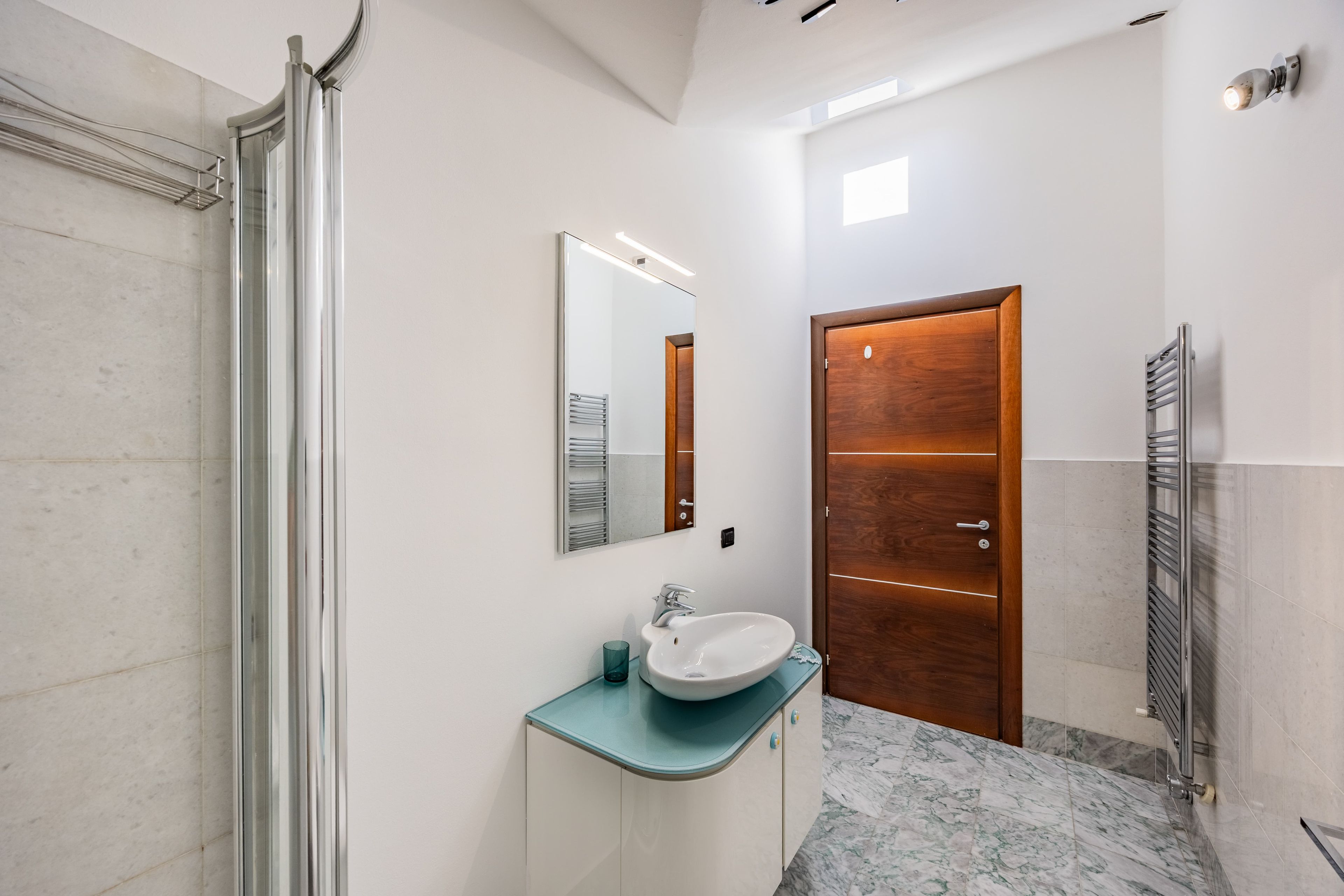 Een moderne badkamer met een glazen douchecabine, een wit wastafelmeubel met een blauw aanrechtblad en een houten deur.
