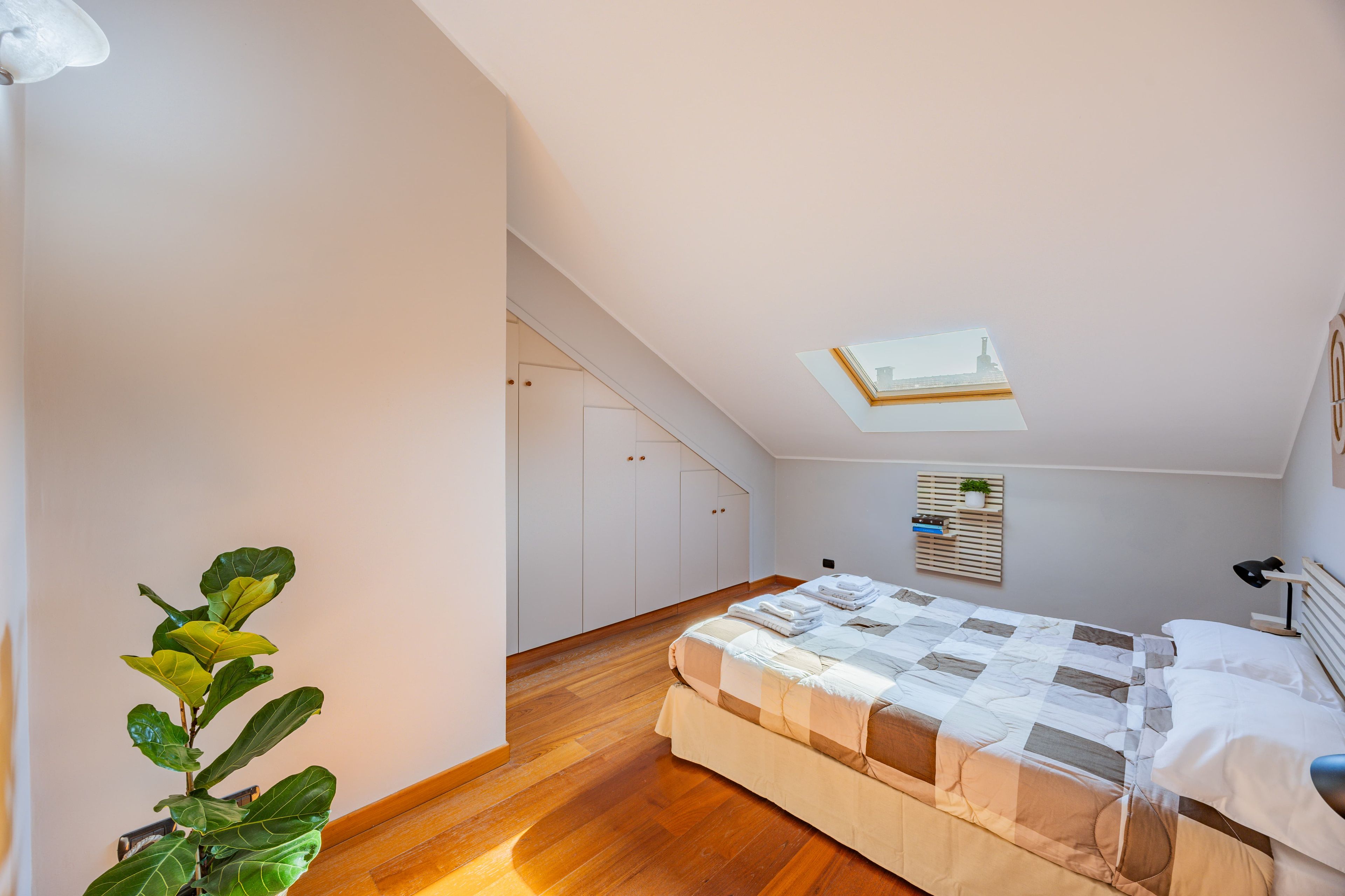 Ein Schlafzimmer mit Bett, Dachfenster, Blumentopf und Holzboden.