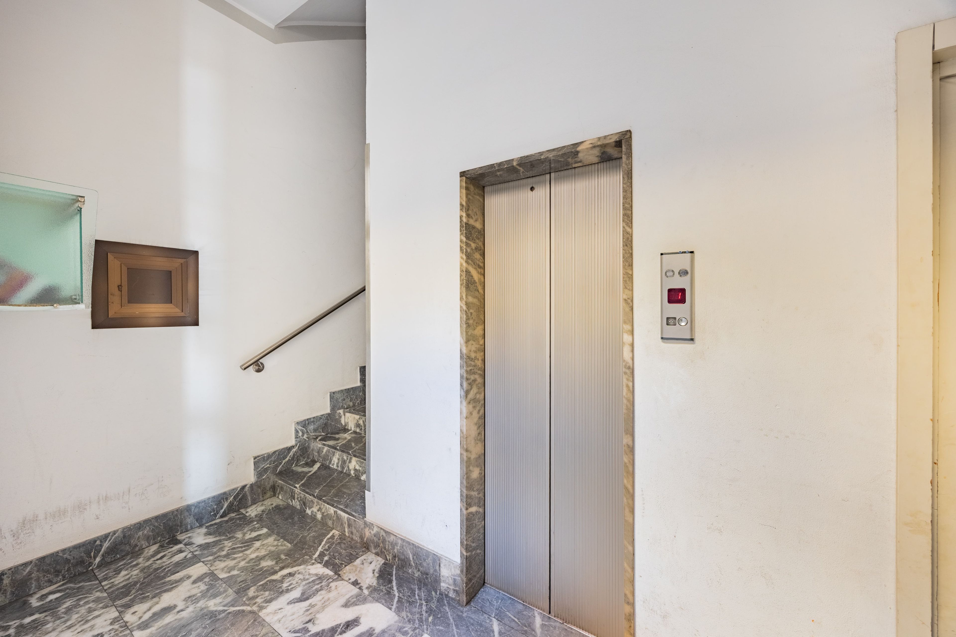 Eine Treppe mit Marmorstufen führt zu einer geschlossenen Elevatortür.