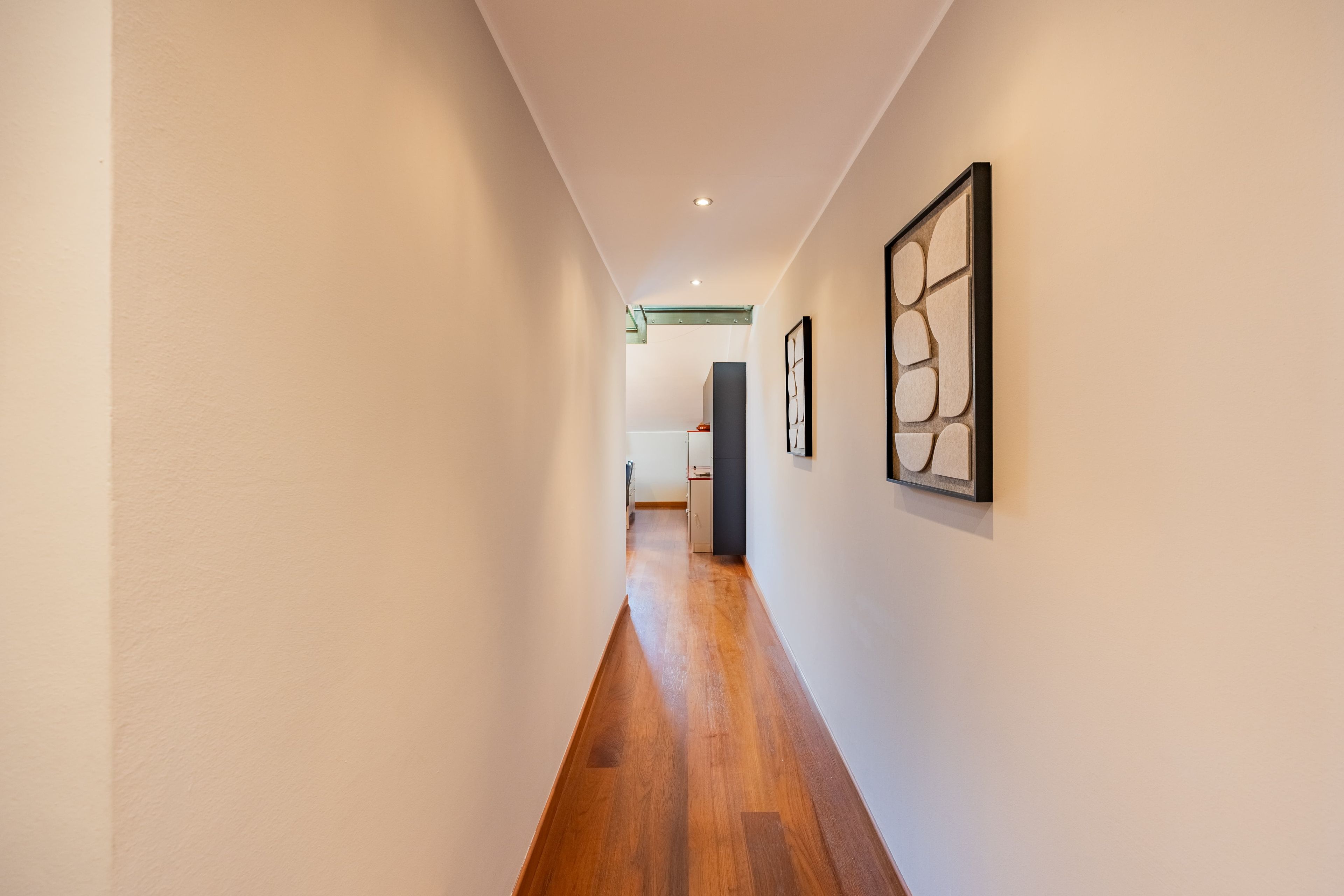 Un couloir doté d’un plancher en bois, de murs blancs et d’œuvres d’art encadrées.