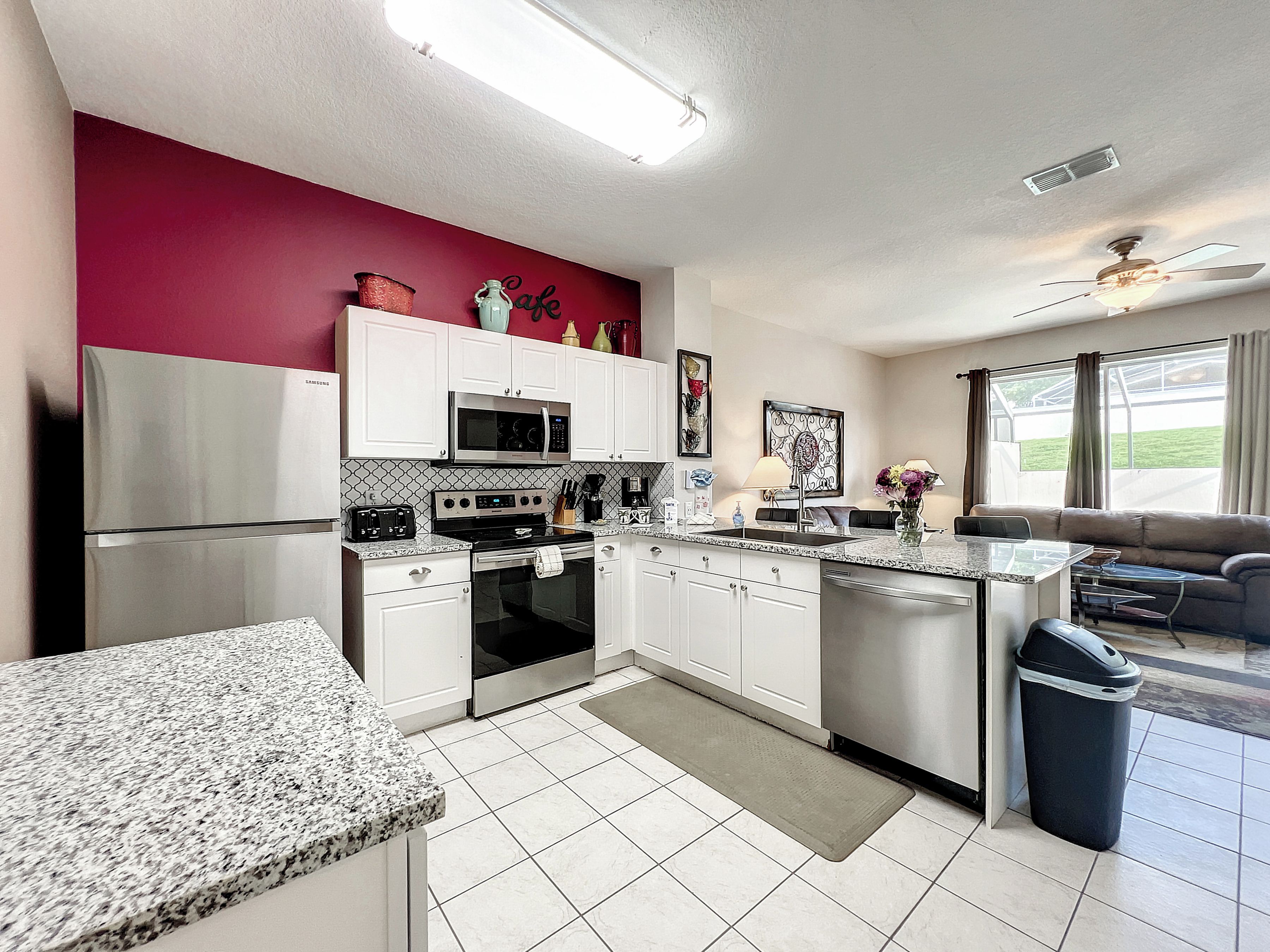 A modern kitchen with white cabinets, a microwave, a stove, and a sink. There is a dining area with a table and chairs.
