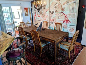 Un coin repas avec une table dressée pour six personnes, entourée de chaises, d’un lustre et d’un grand tableau abstrait accroché au mur.