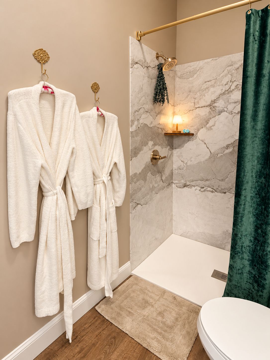 Une salle de bain avec un mur de douche en marbre, une baignoire et deux peignoirs blancs suspendus à des crochets.