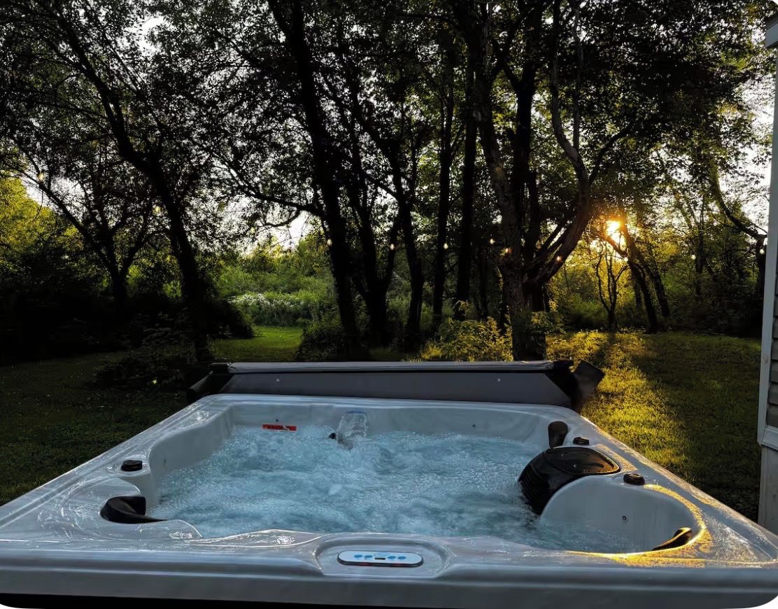 A hot tub outdoors with a natural backdrop of trees and sunlight.