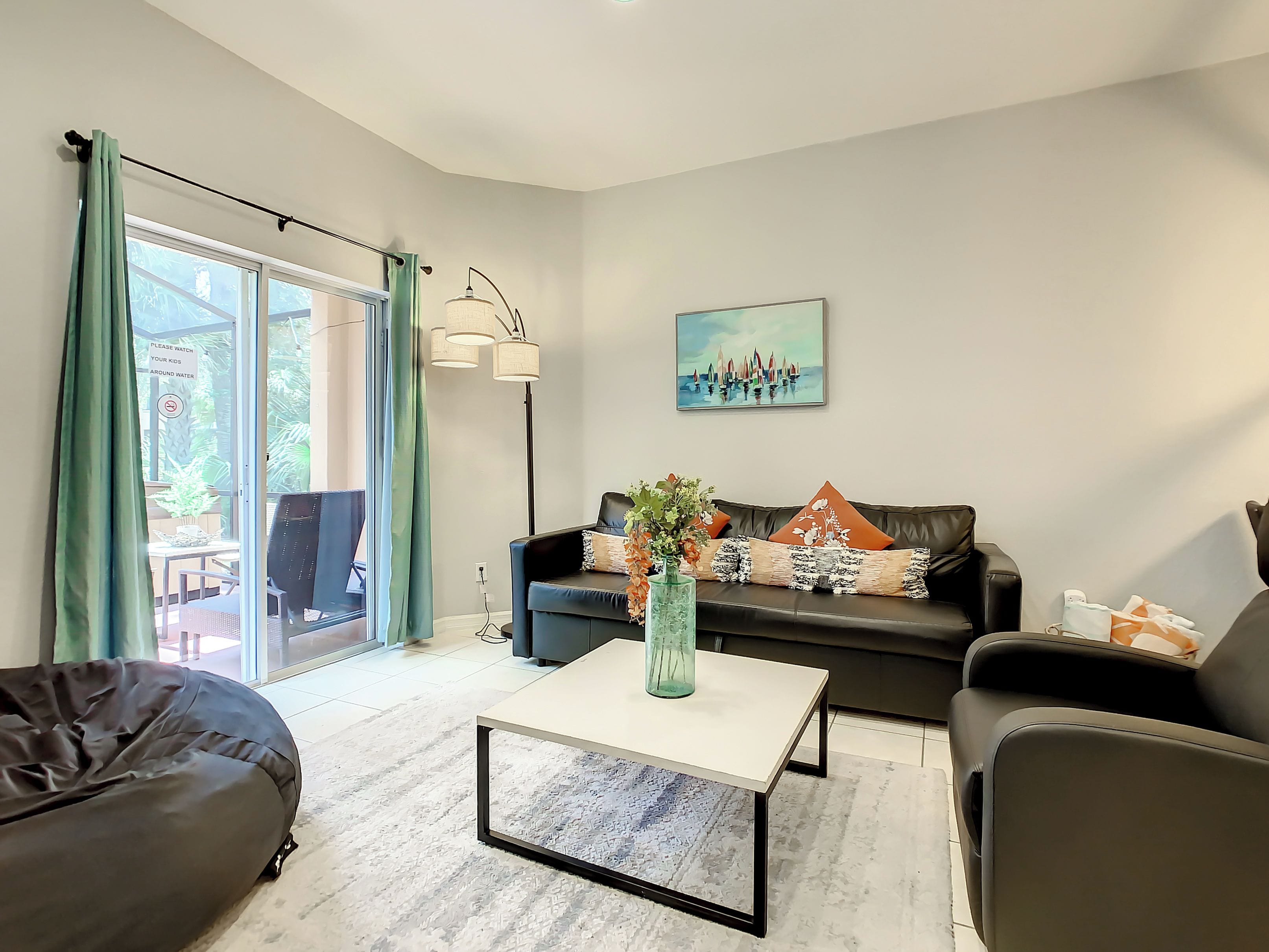 A modern living room with a black leather sofa, a white coffee table, and a glass door leading to a balcony.
