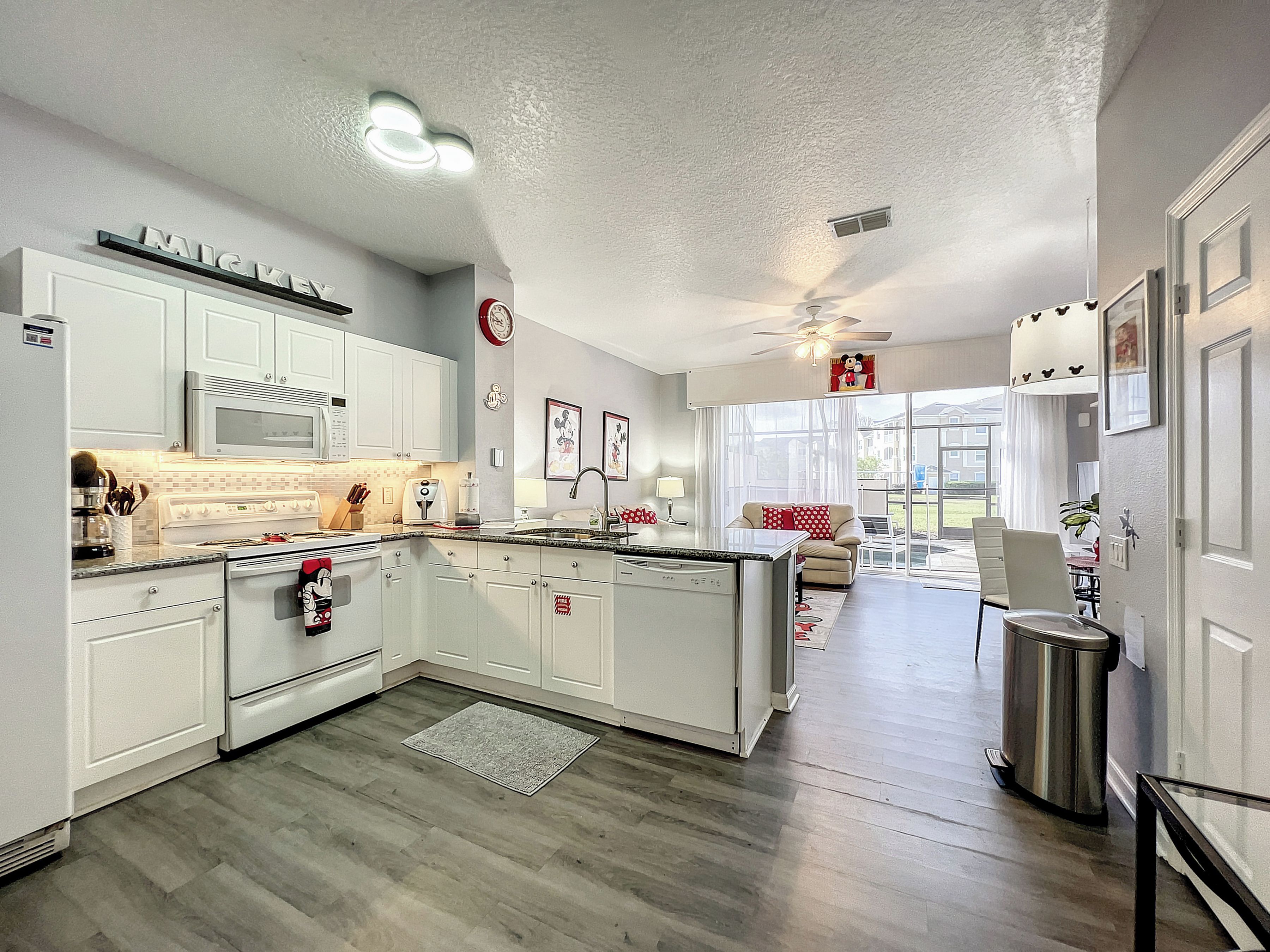 A modern kitchen with white cabinetry, a central island, and a dining area with a sofa and chairs.
