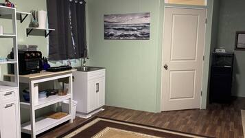 A room with a kitchen area, a white door, a painting of a seascape, and a patterned rug.