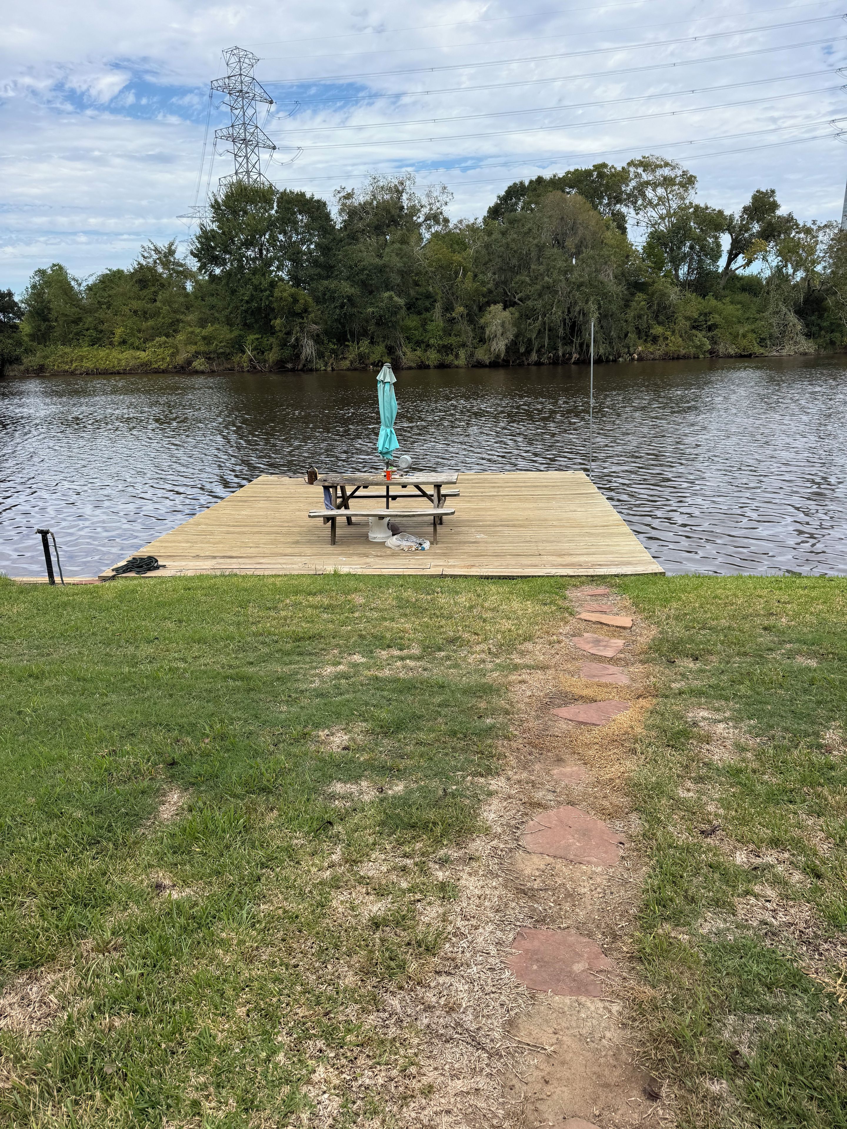 A wooden dock extending into a calm lake, with a picnic table and umbrella in the center.