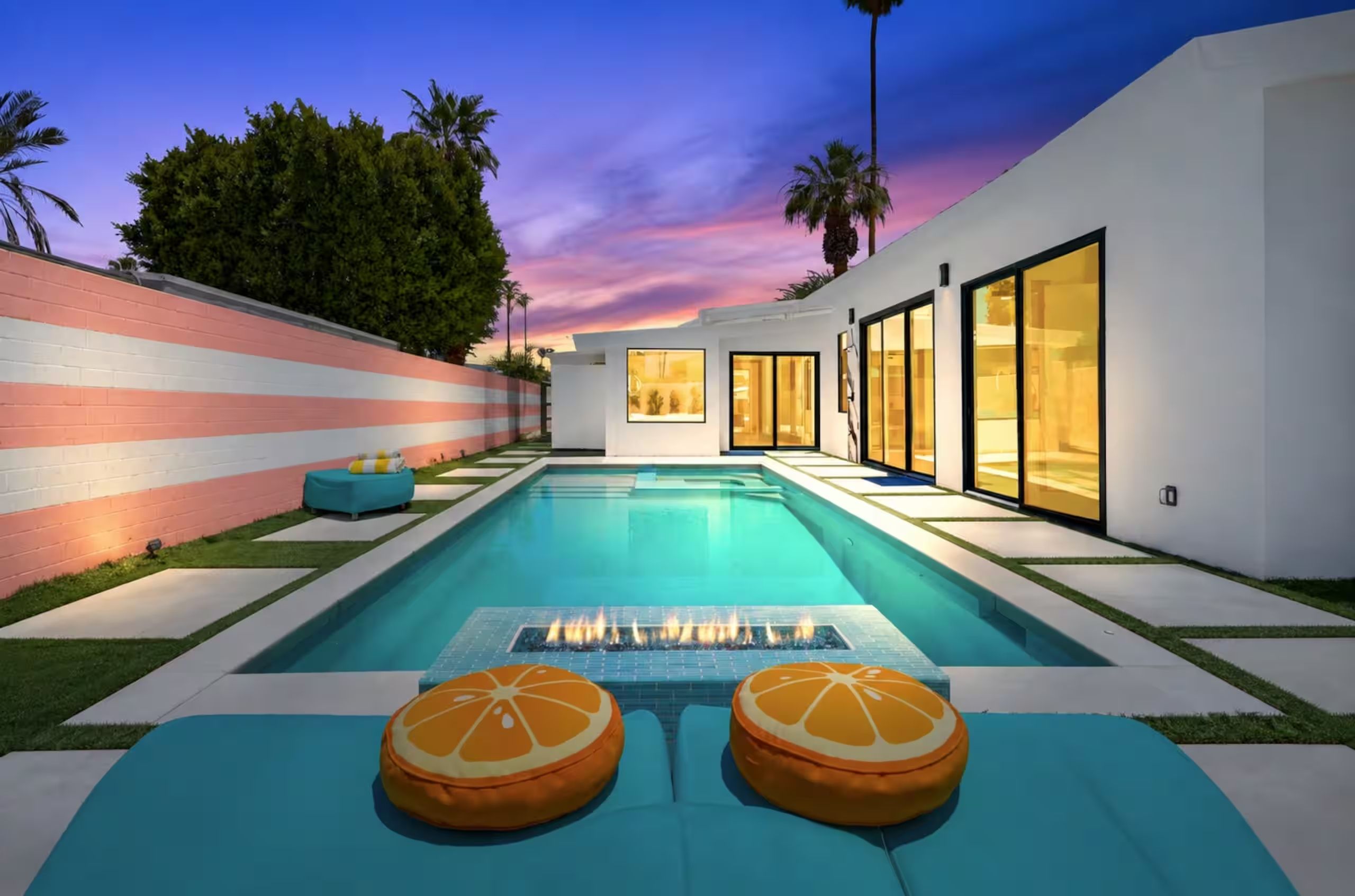 A modern outdoor pool area with a sunset view, a fire feature, and a wall with a striped pattern.