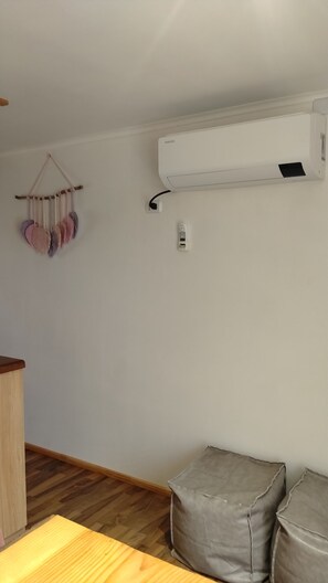 A room with a wooden floor, a white wall-mounted air conditioner, a small table, and two grey cushions. - New Listing (Valdivia)