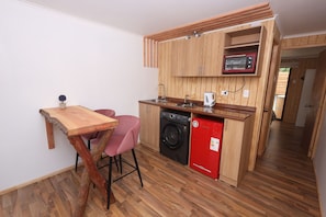 Une cuisine compacte avec des meubles en bois, un four à micro-ondes encastré, un lave-linge et une petite table à manger avec des chaises.