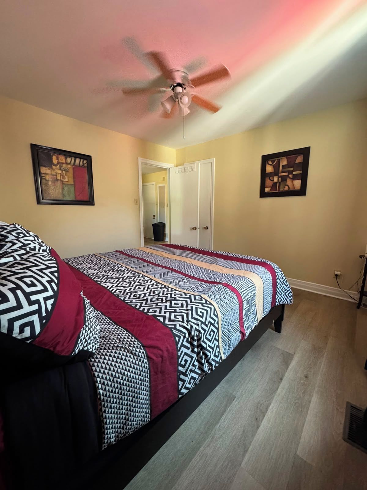 A bedroom with a bed, a ceiling fan, and two framed artworks on the walls.