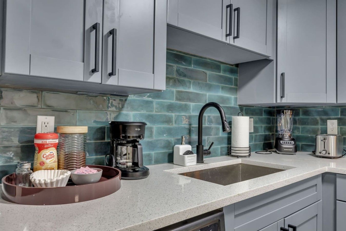 A kitchen with grey cabinets, a coffee maker, a blender, and a toaster.