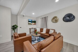 A modern living room with leather sofas, a coffee table, and a painting on the wall. - Sun, Sand & Fire Pit Nights | 3 Blocks to Beach (Jacksonville Beach)