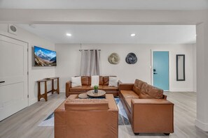 A modern living room with leather sofas, a coffee table, and a flat-screen TV. - Sun, Sand & Fire Pit Nights | 3 Blocks to Beach (Jacksonville Beach)