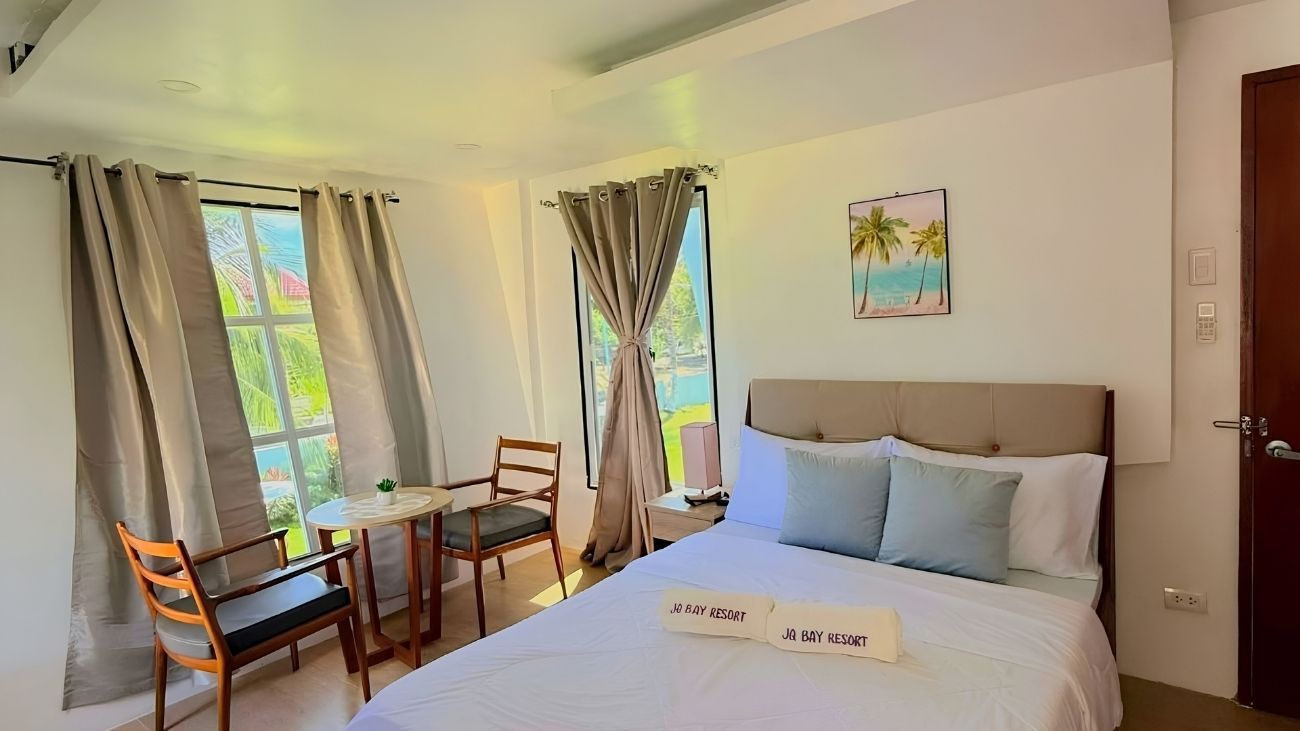 A hotel room with a bed, a desk, a chair, and a window with curtains.