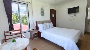 A hotel room with a bed, a bedside table, a chair, a small table with a plant, a TV on the wall, and a window with curtains.