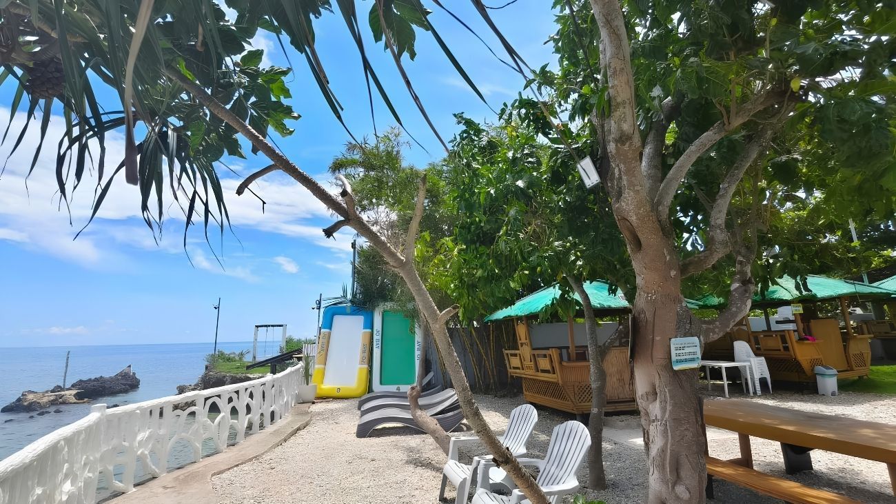 Zona frente al mar con cerca blanca, sillas de playa, una mesa de picnic y un pequeño parque infantil.